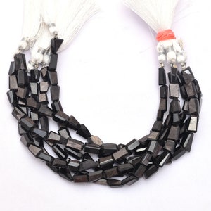 Puede incluir: Una hebra de cuentas de piedras preciosas negras, facetadas y cortadas en forma rectangular. Las cuentas están enhebradas en un cordón blanco y tienen un borla en cada extremo.