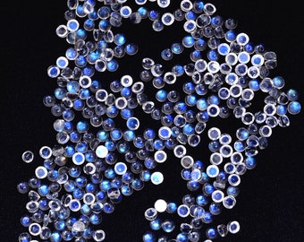 May include: A large group of round, iridescent gemstone cabochons in shades of blue and white. The cabochons are scattered on a black background.