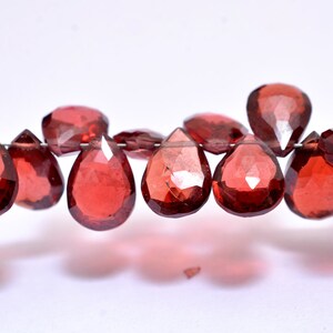 May include: A strand of faceted red gemstone beads in a teardrop shape. The beads are strung on a silver wire.