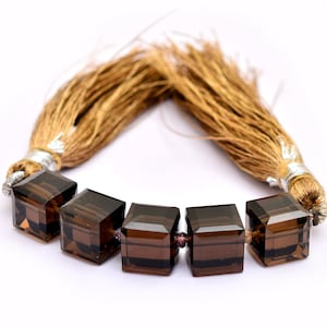 May include: A strand of six brown smoky quartz gemstone beads, each cut into a square shape. The beads are strung on a brown cord with tassels on each end.