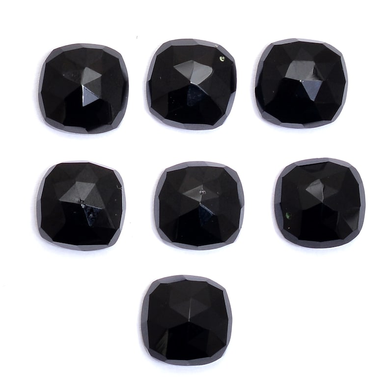May include: Seven black cushion-cut gemstones with a faceted finish. The gemstones are arranged in a staggered pattern on a white background.