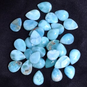 May include: A collection of 25 teardrop-shaped blue and white gemstone cabochons. The cabochons are smooth and polished, with a pearlescent sheen.