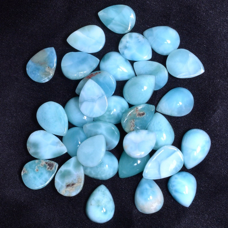 May include: A collection of 25 teardrop-shaped blue and white gemstone cabochons. The cabochons are smooth and polished, with a pearlescent sheen.