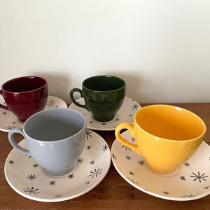 May include: Four teacups and saucers with a snowflake pattern. The cups are in shades of red, green, blue, and yellow.