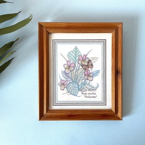 May include: A framed botanical illustration of a wild pansy, also known as Viola tricolor, with delicate purple and pink flowers and green leaves. The illustration is titled "Wild Pansy" and includes the scientific name "Viola tricolor" and the family name "Violaceae".