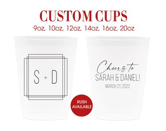 May include: Two white plastic cups with custom designs. The cup on the left has a black square frame with the letters "S + D" inside. The cup on the right has the text "Cheers to SARAH & DANIEL! MARCH 21, 2022".