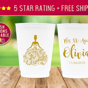 May include: Two white plastic cups with gold lettering. One cup features a gold silhouette of a woman in a ball gown with floral designs. The other cup says "Mis XV A&ntilde;os Olivia 11/24/2018".