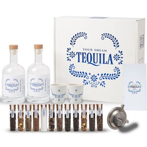 May include: A white box with the words "Your Dream Tequila" in blue lettering. The box contains two clear glass bottles of tequila, two white ceramic shot glasses with blue floral designs, a strainer, and 16 small glass vials filled with various ingredients.