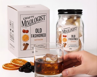 May include: A white box and a glass jar labeled "Crafty Mixologist Old Fashioned Infusion" with illustrations of cherries, orange slices, and cinnamon sticks. A glass of amber liquid with a large ice cube is held by a hand. Dried orange slices and cherries are in front.