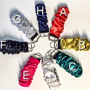 May include: Eight keychains with different coloured fabric covers. The keychains are arranged in a circle with the fabric covers facing outwards. The keychains are labelled with letters A through H.