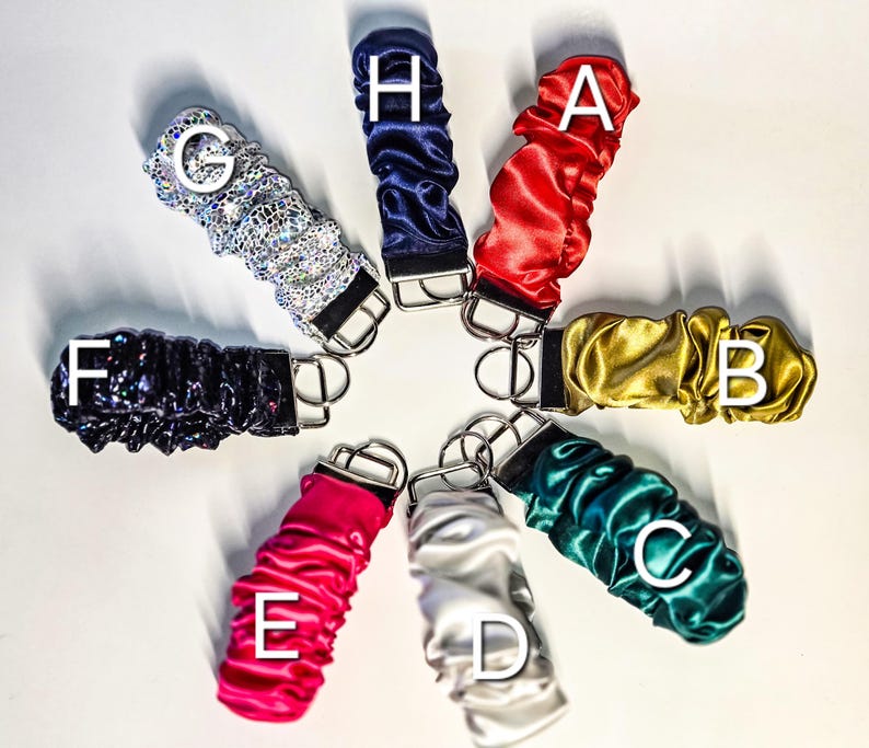 May include: Eight keychains with different coloured fabric covers. The keychains are arranged in a circle with the fabric covers facing outwards. The keychains are labelled with letters A through H.