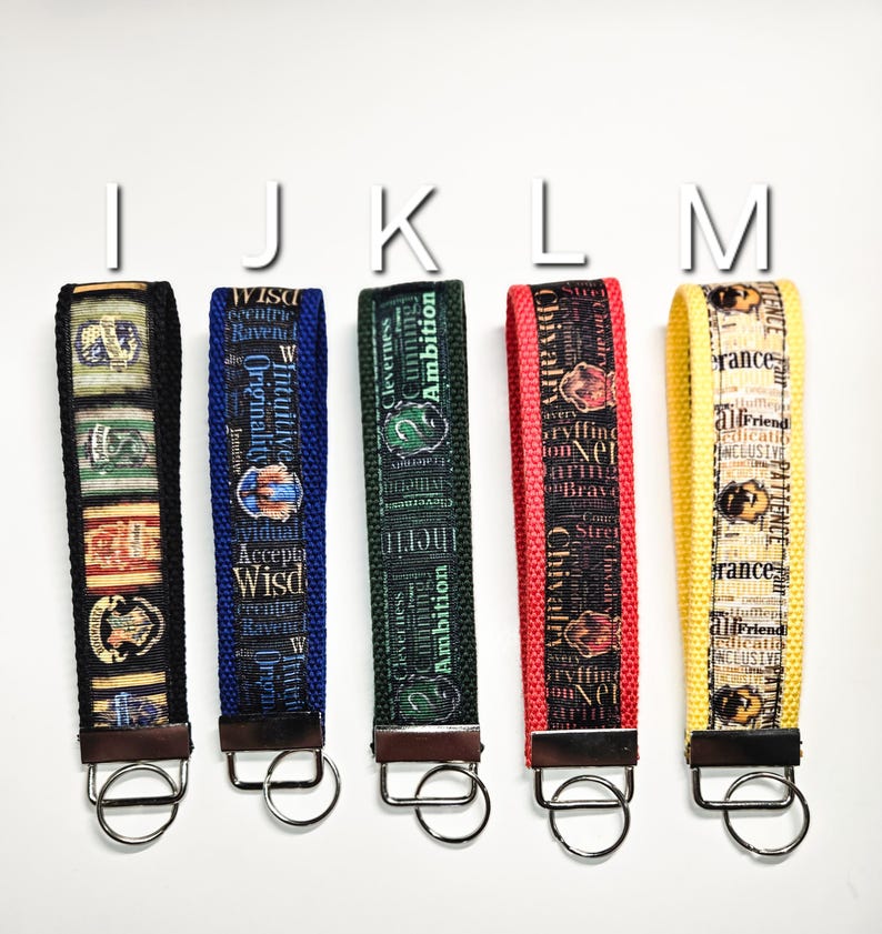May include: Five colourful keychains with different house crests from the Harry Potter universe. Each keychain features a different house crest and a key ring. The keychains are blue, green, red, and yellow.
