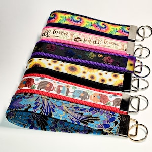 May include: A stack of colourful keychains with different patterns and designs. The keychains feature tie-dye, sunflowers, elephants, and a floral pattern. Each keychain has a gold metal ring.