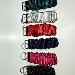 May include: A set of ten keychains with different coloured satin fabric covers. The keychains are all the same size and shape, and they have a silver metal ring.