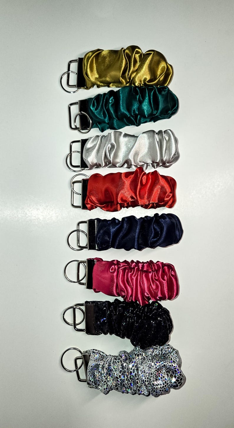 May include: A set of ten keychains with different coloured satin fabric covers. The keychains are all the same size and shape, and they have a silver metal ring.