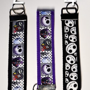 May include: Three keychains with different designs featuring the character Jack Skellington from the movie The Nightmare Before Christmas. The keychains are black, purple, and black with white designs. The keychains are numbered 2, 3, and 4.