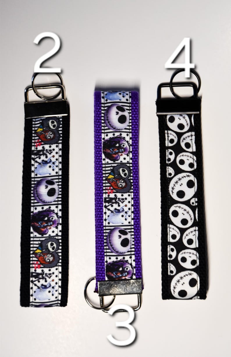 May include: Three keychains with different designs featuring the character Jack Skellington from the movie The Nightmare Before Christmas. The keychains are black, purple, and black with white designs. The keychains are numbered 2, 3, and 4.