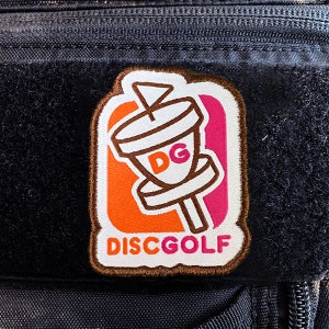 May include: A brown, orange, and pink embroidered patch with a disc golf basket and the text "DISCGOLF".