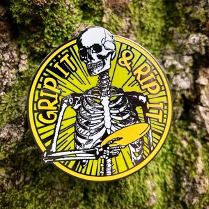 May include: A yellow and black enamel pin featuring a skeleton holding a disc with the text "GRIP IT & RIP IT" around the edge.