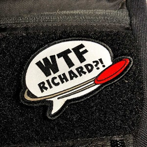 May include: A white speech bubble patch with the text "WTF RICHARD?!" in black lettering. A red and gray disc is behind the speech bubble.