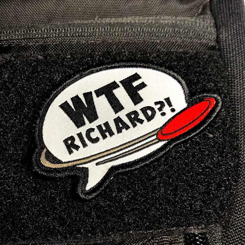 Pode incluir: Um remendo de bolha de fala branca com o texto "WTF RICHARD?!" em letras pretas. Um disco vermelho e cinza est&aacute; atr&aacute;s da bolha de fala.
