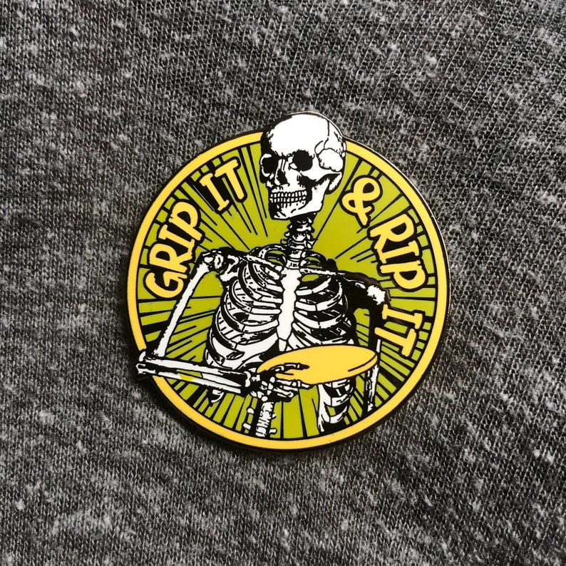May include: A yellow and black enamel pin featuring a skeleton holding a frisbee with the text "Grip It & Rip It" around the edge.
