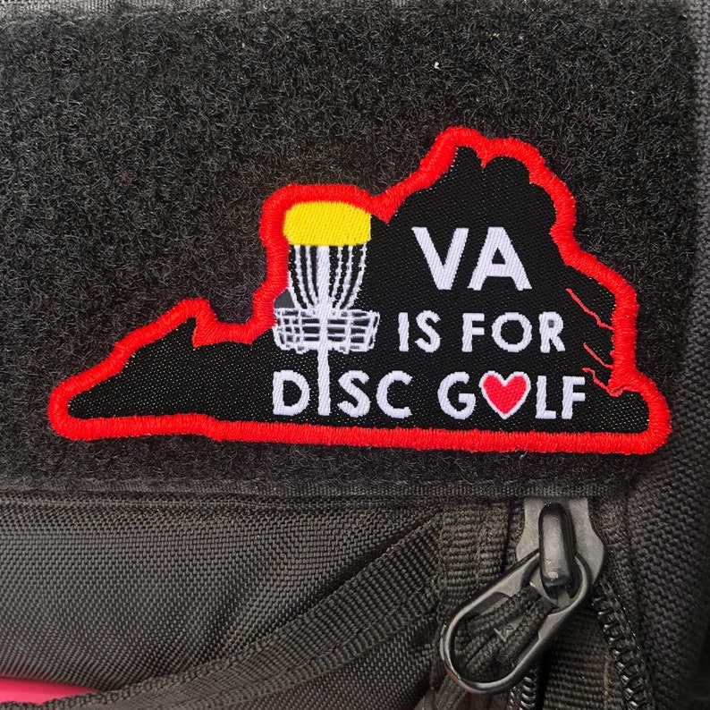 K&ouml;nnte beinhalten: Ein schwarzer und roter Patch mit der Umrandung des Bundesstaates Virginia. Der Patch sagt "VA is for DISC GOLF" mit einem roten Herzen anstelle des "O".