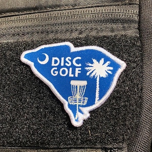 May include: A blue and white embroidered patch shaped like the state of South Carolina with the words "DISC GOLF" and a disc golf basket.