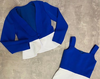 May include: A blue and white two-piece outfit. The top is a cropped blazer with long sleeves and a white trim. The bottom is a white skirt with a blue top.