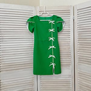 May include: A bright green dress with white trim and bow details. The dress features a square neckline, short sleeves, and a slit on the side. The bows are white and are used as a decorative element.