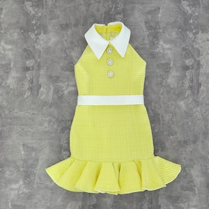 May include: A yellow halter dress with a white collar and a white belt. The dress has three pearl buttons and a ruffled hem. The fabric has a textured appearance.