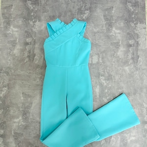 May include: A light blue jumpsuit with a criss-cross halter neckline and wide legs.