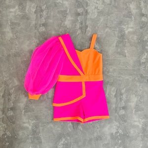 May include: A vibrant, one-shoulder romper in bright pink and orange. The design features a single, voluminous pink mesh sleeve, a contrasting orange bodice, and pink shorts with orange trim. The outfit is set against a gray background.