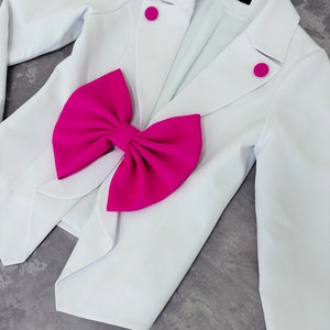 May include: A white blazer with a large, bright pink bow and matching pink buttons. The blazer has a classic tailored design, with a notched lapel and long sleeves. The bow is a prominent feature, adding a bold pop of color.