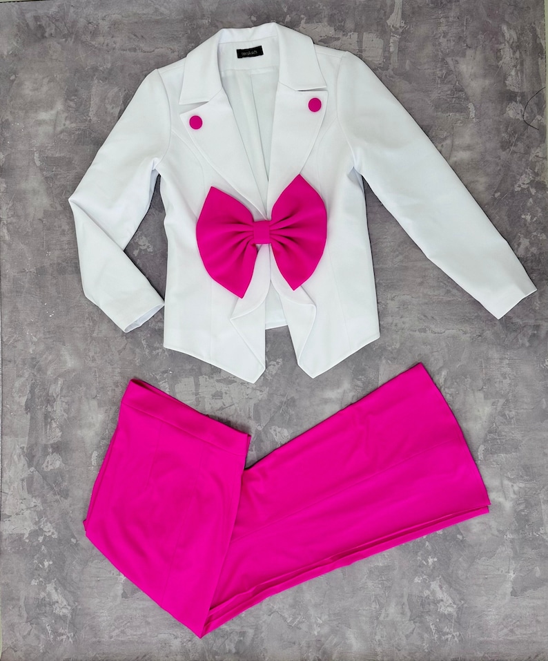May include: A white blazer with a large fuchsia bow and matching fuchsia pants. The blazer has two fuchsia buttons and a tailored fit. The pants are a straight-leg style.