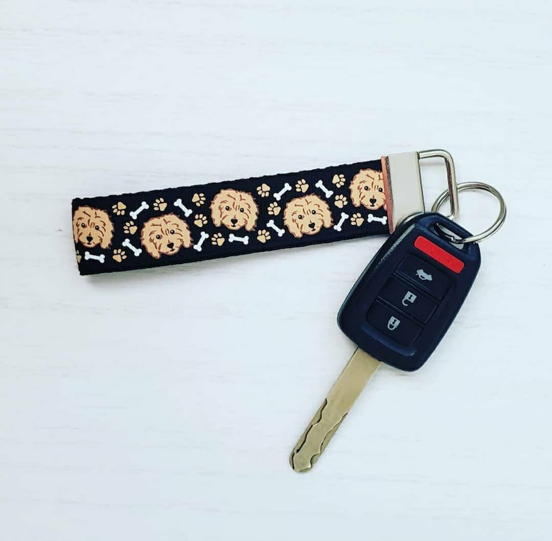 May include: Black and white key chain with a repeating pattern of brown dog faces and white bone shapes. The key chain is attached to a black car key with a red button.