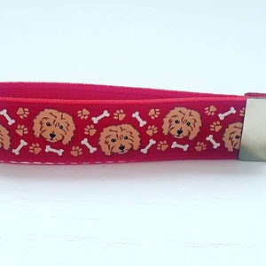 May include: Red key chain with a repeating pattern of brown dog faces, white bones, and orange paw prints. The key chain has a silver metal ring.