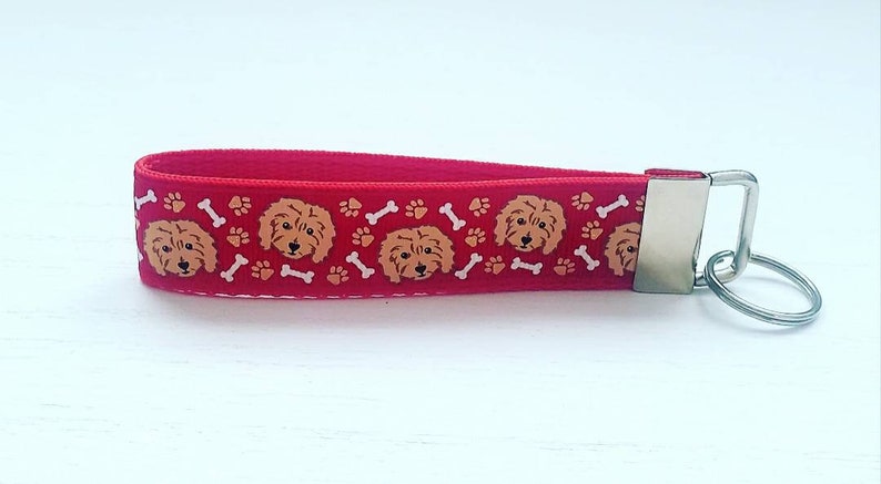 May include: Red key chain with a repeating pattern of brown dog faces, white bones, and orange paw prints. The key chain has a silver metal ring.