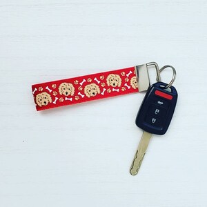 May include: Red and white key chain with a pattern of dog faces and paw prints. The key chain is attached to a silver key ring and a black car key.