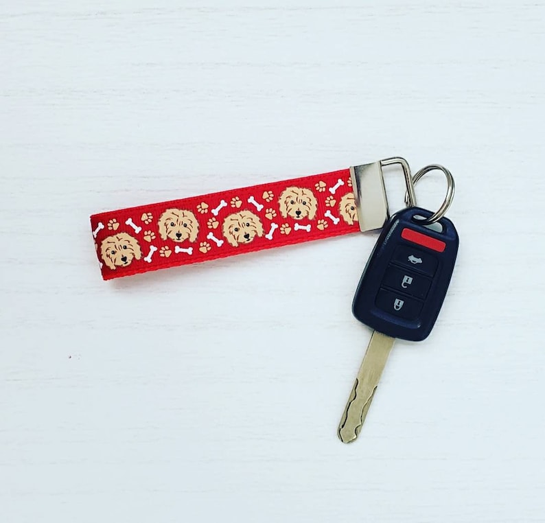 May include: Red and white key chain with a pattern of dog faces and paw prints. The key chain is attached to a silver key ring and a black car key.