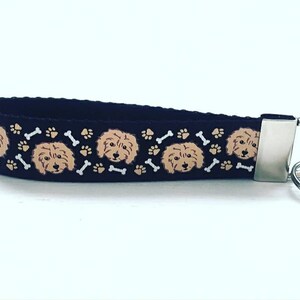 May include: A black key chain with a repeating pattern of brown and white dog faces and bone shapes. The key chain has a silver metal ring.