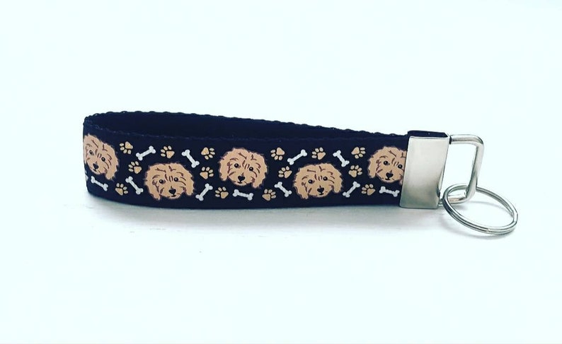 May include: A black key chain with a repeating pattern of brown and white dog faces and bone shapes. The key chain has a silver metal ring.
