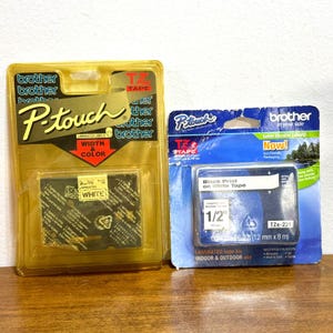 以下が含まれることがあります： 2つのBrother P-touchラベルメーカーテープカートリッジ。1つは白いテープが入った金色のパッケージ、もう1つは白いテープに黒い印刷がされた青色のパッケージです。青色のカートリッジは幅12mmです。