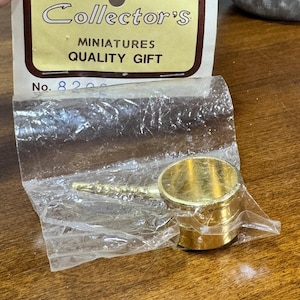 May include: A miniature gold-colored saucepan with a long handle, packaged in clear plastic. The packaging includes the text "Collector's", "MINIATURES", and "QUALITY GIFT". The item is a miniature collectible.