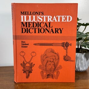 Puede incluir: Un libro naranja titulado "Melloni's Illustrated Medical Dictionary" con texto blanco. La portada presenta ilustraciones de herramientas médicas y un feto. El libro está de pie sobre una superficie de madera.