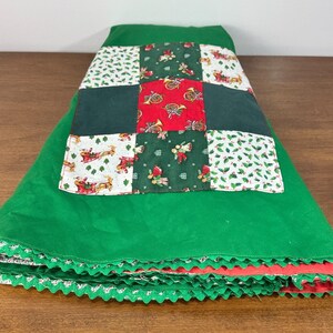 May include: A green fabric tree skirt featuring a central patchwork panel with alternating squares of red, dark green, and white fabric printed with holiday motifs including Santa Claus in a sleigh, holly leaves, and musical instruments.