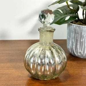 May include: A white ceramic mug with a black handle and the text "But First, Coffee" in a handwritten style. The mug is on a white surface. The mug is approximately 4 inches tall.