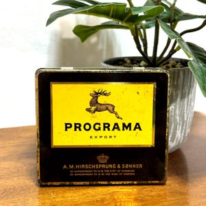以下が含まれることがあります： 黒い持ち手と「But First, Coffee」のテキストが黒い太字で書かれた白いセラミックマグ。マグカップには濃い液体、おそらくコーヒーが入っており、明るい色の表面に置かれています。