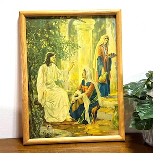 Puede incluir: Una impresión religiosa enmarcada que representa una escena bíblica. La obra presenta figuras con túnicas fluidas, con una figura central gesticulando. La paleta de colores incluye amarillos, azules y verdes suaves, enmarcada en un marco de madera marrón claro.
