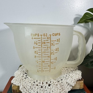 Könnte beinhalten: Ein Vintage, durchscheinender Messbecher mit Griff und Ausguss. Der Becher hat braune Markierungen für Tassen und Unzen, mit Messungen bis zu 4 Tassen und 946 ml. Der Becher besteht aus einem mattierten, halbtransparenten Material.